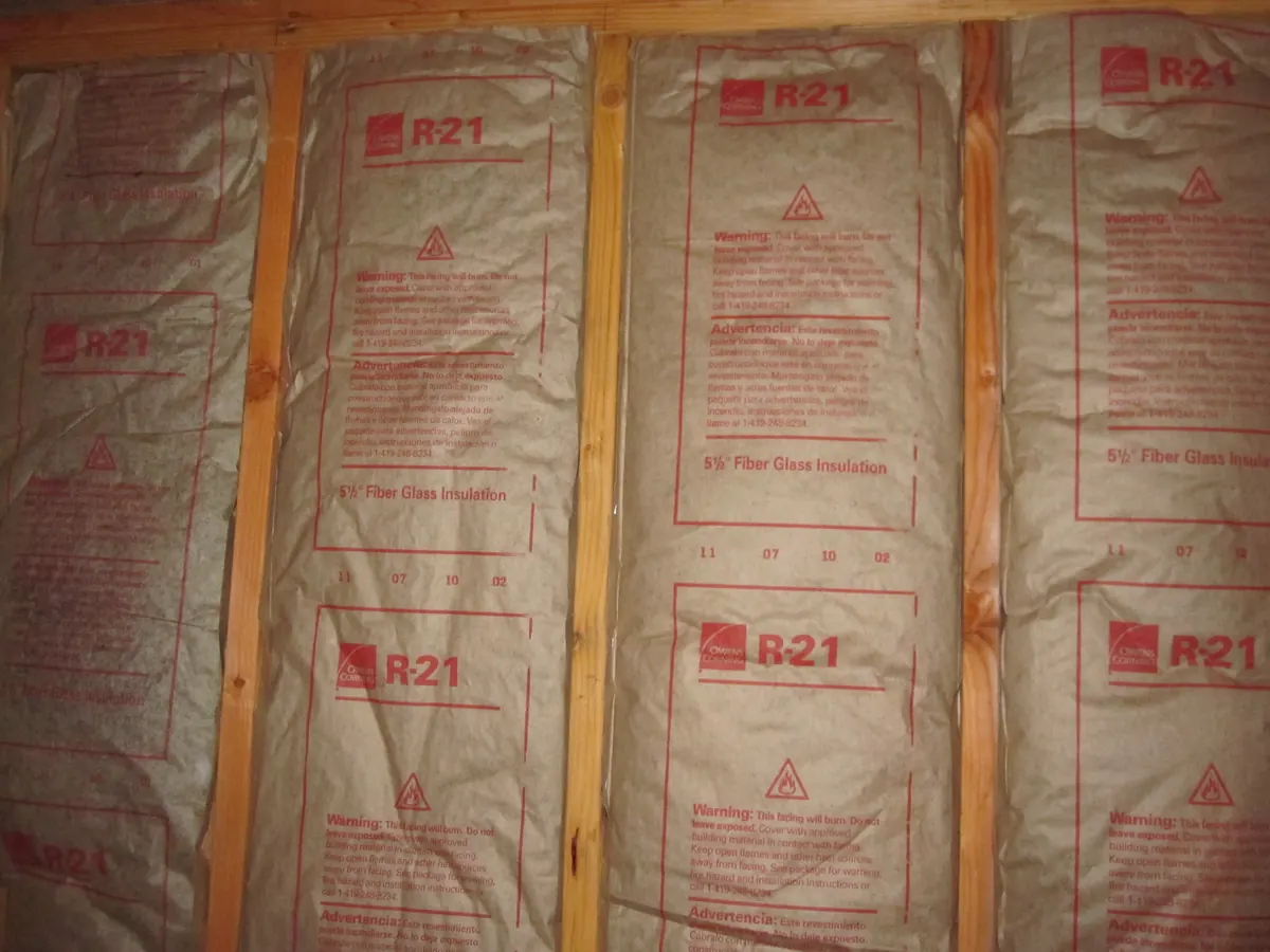 Kraft-faced fiberglass batts installed between wall studs, with printed R-value labeling visible on the paper facing