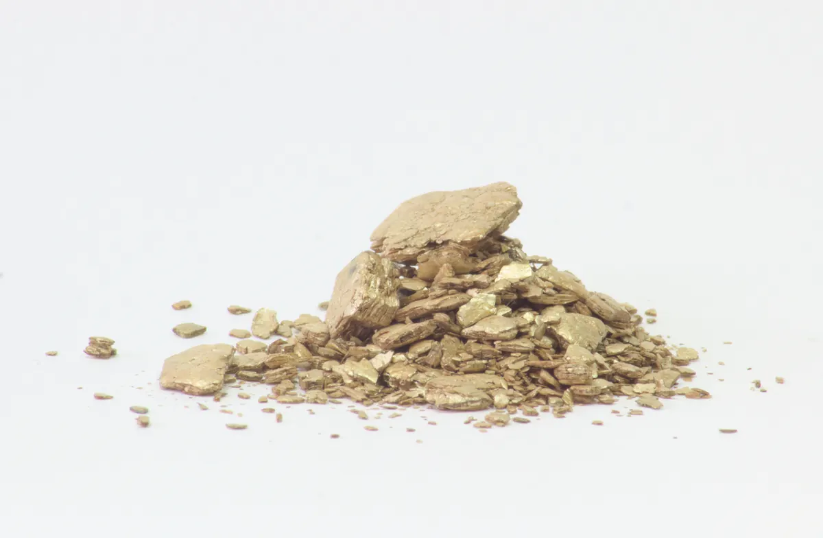 A small pile of golden-brown vermiculite flakes with a layered, glittery texture on a white background